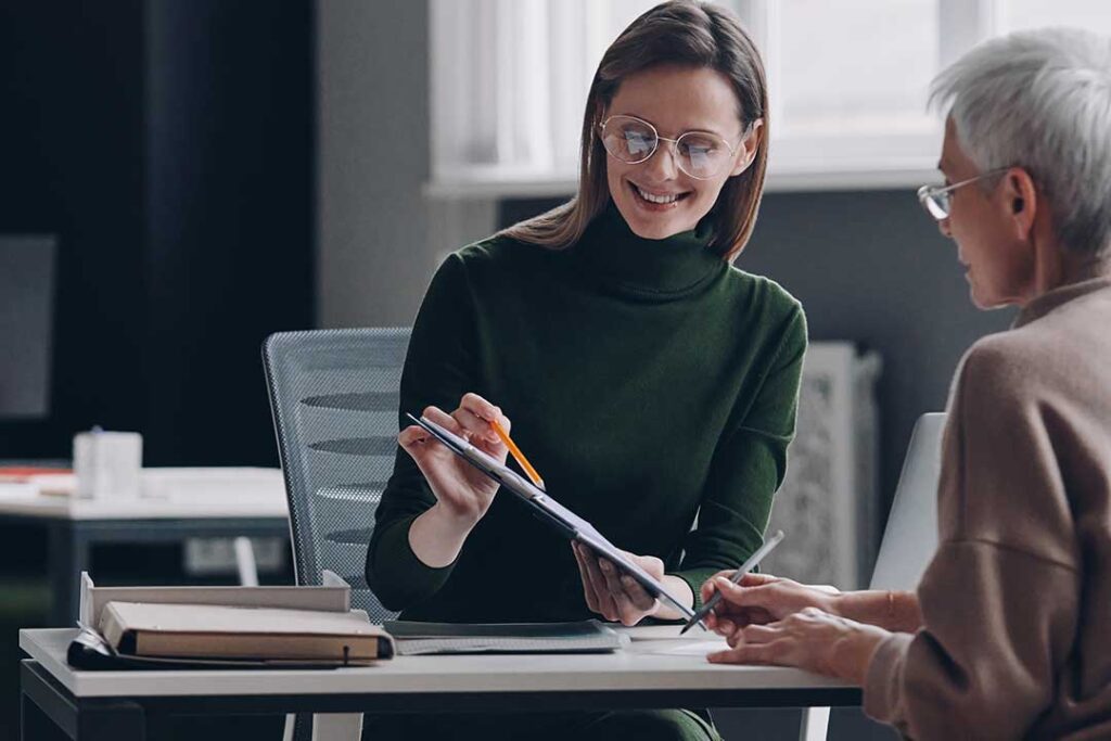 A person sitting at a kitchen table reviewing home insurance documents with a laptop and notepad.