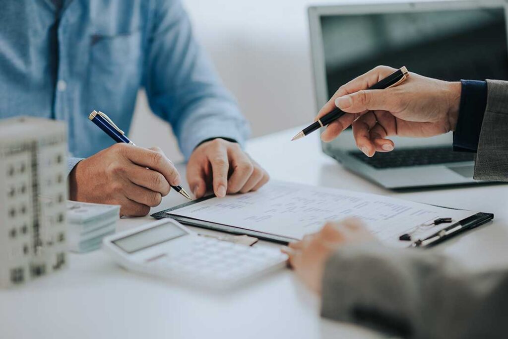 An insurance adjuster reviews accident photos and claim documents with a homeowner at a kitchen table.